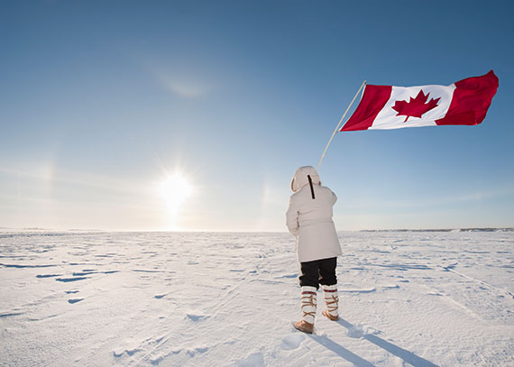 A woman holds the Canadian flag while gazing at a sunrise in the northwest territories, symbolizing a new day and hope for success in alcohol rehab