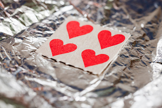 This photo depicts a small, white square with four hearts evenly distributed within it. The small square is laying diagonally on a piece of aluminium foil; with a few crinkles.